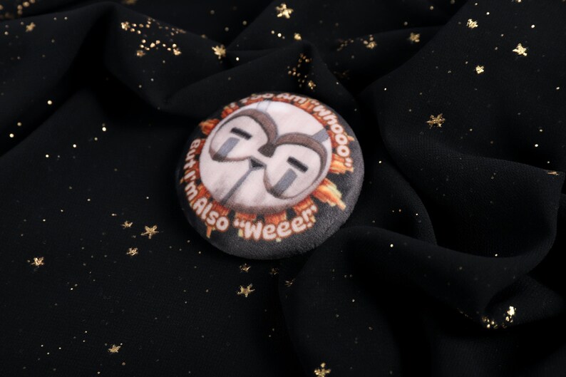 A squishy plush pin of Esquie from Expedition 33- It features Esquie's head from Clair Obscur Expedition 33 featuring the text: "I am too "Whooo" but I am also "Wheee"