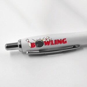 May include: White pen with a black grip and a bowling ball and pins graphic with the word "BOWLING" in red letters.