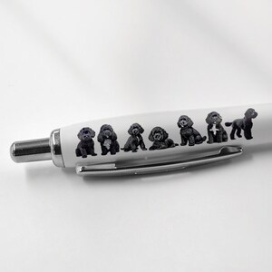 May include: A white ballpoint pen with a black rubber grip and silver detailing. The pen's barrel is decorated with a series of small, black dog illustrations. The pen is designed for writing.