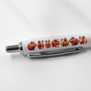 May include: A white pen with a black rubber grip and a line of brown guinea pigs printed on the barrel.