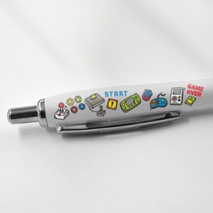 May include: White pen with a black cap and a design of video game icons and the words "START" and "GAME OVER".