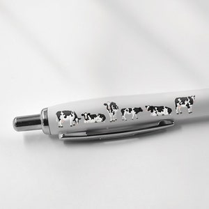 May include: A white pen with a black grip and a design of black and white cows on the barrel.