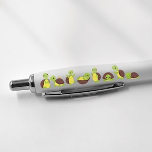 May include: A white pen with a black grip and a line of small green turtles printed on the barrel.