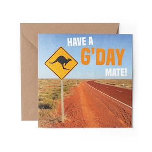 May include: A greeting card with a yellow road sign featuring a black kangaroo. The sign reads "Have a G'day Mate!" The background is a photo of a red dirt road in the Australian outback.