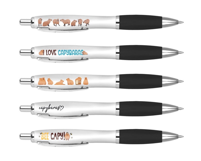 May include: Five white pens with black caps and different capybara-themed designs. The designs include capybaras in various poses, the text "I LOVE CAPYBARAS", "capybaras", and "BEE CAPY!"