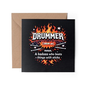May include: A black greeting card featuring the word "DRUMMER" in a flame-like design. The card defines a drummer as "A badass who beats things with sticks." The card is in a brown envelope.
