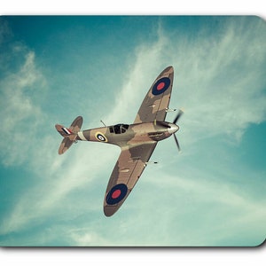 May include: A vintage-style photo of a green, brown, and grey camouflage World War II era fighter plane flying in a blue sky with white clouds. The plane has red, white and blue roundels on the wings.