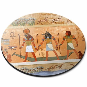 May include: A round mouse mat featuring a colourful illustration of three Egyptian gods in a boat. The gods are depicted in a traditional style with hieroglyphs and symbols. The background is a warm orange colour with a faded texture.