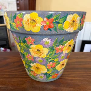 May include: A hand-painted terracotta flower pot with a blue glaze. The pot is decorated with yellow, red, and purple flowers and green leaves.