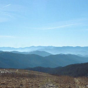 Peut inclure: Vue panoramique d'une chaîne de montagnes avec un ciel bleu brumeux. Les montagnes sont superposées au loin, créant une impression de profondeur et de perspective.