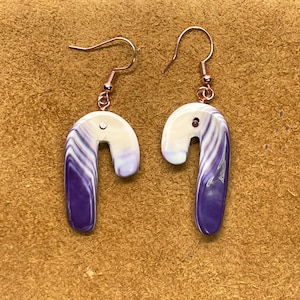 Könnte beinhalten: Ein Paar Ohrringe mit einem Design aus lila und weißer Muschel. Die Ohrringe sind aus Metalldraht gefertigt und haben einen Hakenverschluss.