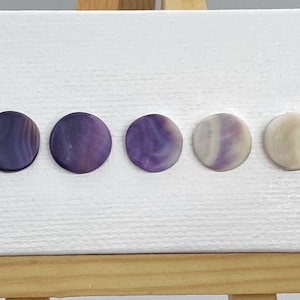 May include: Five round, flat, decorative buttons with a purple and white marbled pattern. The buttons are arranged in a row on a white surface.