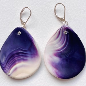 Könnte beinhalten: Ein Paar tropfenförmige Ohrringe mit einem wirbelnden Muster in Lila, Weiß und Creme. Die Ohrringe haben silberfarbene Klappbügelverschlüsse. Ein Modeaccessoire.