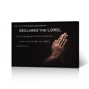 May include: A black canvas print with a white inspirational quote from Jeremiah 29:11. The quote reads "For I know the plans I have for you declares the Lord, plans to prosper you and not to harm you, plans to give you hope and a future." The quote is centered on the canvas with a pair of hands clasped in prayer on the right side of the canvas.