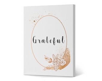 May include: A white canvas print with the word "Grateful" in black script within a copper-colored oval frame. The design includes copper-colored floral and leaf accents, and gold speckles.