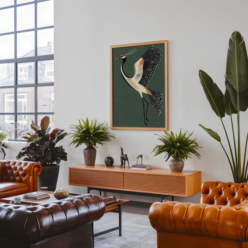 May include: A framed illustration of a stylized crane with black, white, and orange accents against a dark green background. The crane is depicted with its wings spread, and its head is turned to the side. The illustration is framed in a natural wood frame.