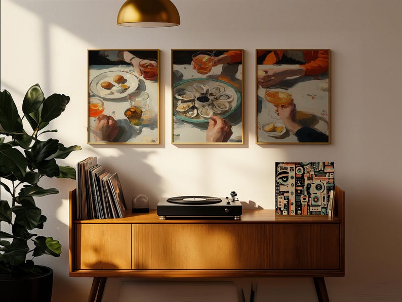 Pu&ograve; includere: Tre stampe artistiche incorniciate raffiguranti una scena di ristorazione con cibo e bevande. Le stampe sono appese sopra un mobile in legno con un giradischi e dischi in vinile. Una grande pianta verde &egrave; nell'angolo.