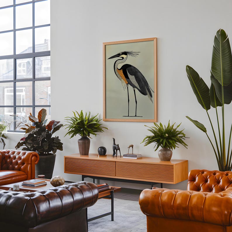 Puede incluir: Una ilustraci&oacute;n enmarcada de un p&aacute;jaro gris y negro con acentos naranjas de pie sobre un fondo azul claro. El p&aacute;jaro est&aacute; enmarcado en un marco de madera claro y est&aacute; colgado en una pared blanca. La pared est&aacute; decorada con plantas y un estante de madera con algunos art&iacute;culos decorativos.