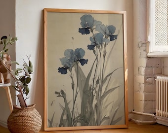 May include: A framed botanical print depicting blue iris flowers and green leaves on a cream backdrop. The artwork is in a light brown wooden frame. The print is leaning against a white wall and wooden floor.