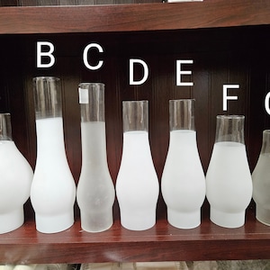 May include: Eight frosted glass lampshades of varying sizes and shapes, labeled A through G. The lampshades are arranged in a row on a wooden shelf.
