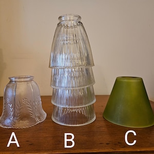 May include: Three glass lampshades, one with a clear ribbed design, one with a clear floral pattern, and one with a solid green color. The lampshades are labeled A, B, and C.