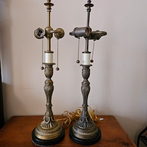 May include: Two antique table lamps with ornate bases and shades. The lamp on the left has a gold finish, while the lamp on the right has a darker bronze finish.