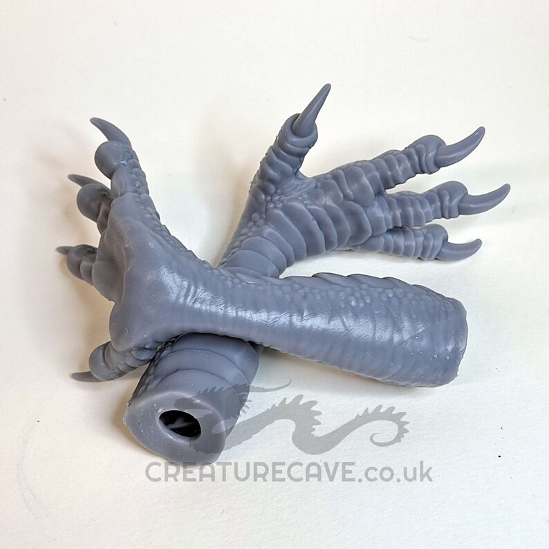 May include: Gray 3D printed dragon foot with claws. The foot is designed to be hollow and has a hole in the bottom for attaching to a base.
