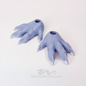 May include: Two gray 3D printed plastic claws with holes in the top. The claws are designed to be used as a prop or costume accessory.