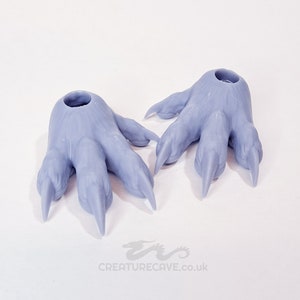 Puede incluir: Dos pies de monstruo articulados de plástico gris claro impresos en 3D con garras. Los pies están diseñados para ser utilizados como accesorio de disfraz o de utilería.