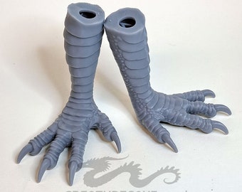 May include: A pair of grey, 3D printed, dragon feet with claws. The feet are posed as if walking. The feet are hollow and have a hole at the top for attaching to a larger model.