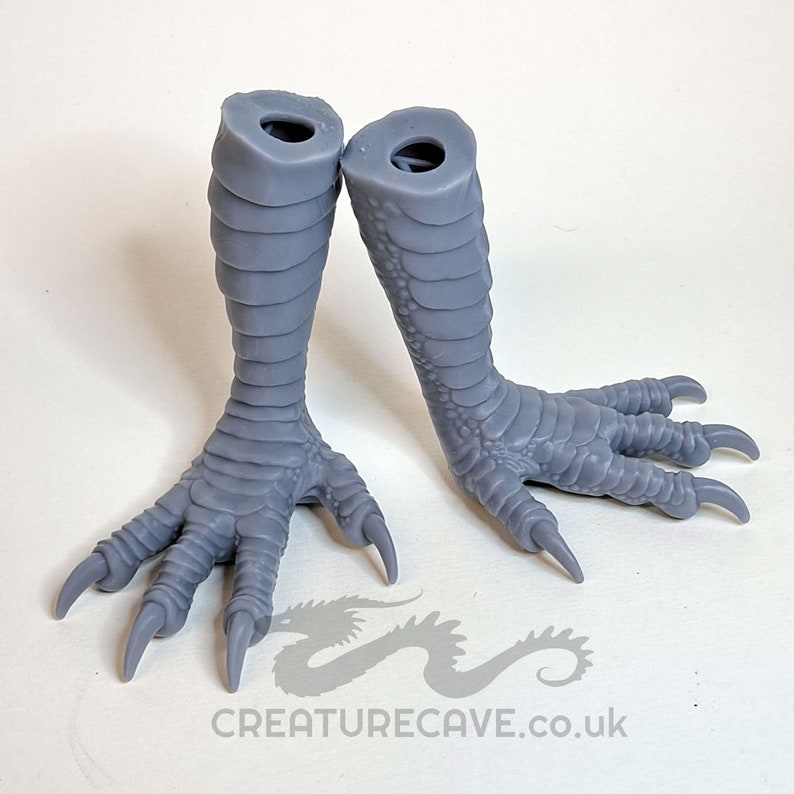 May include: A pair of gray, 3D printed, dragon feet with claws. The feet are posed as if walking. The feet are hollow and have a hole at the top for attaching to a larger model.