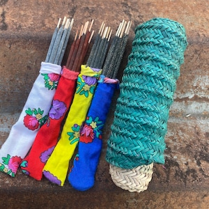 Peut inclure: Un assortiment de bâtonnets d'encens dans des étuis en tissu colorés à motifs floraux. Les étuis sont blancs, rouges, jaunes et bleus. Un récipient vert tressé est également présent, suggérant un thème d'aromathérapie ou de parfum d'intérieur.