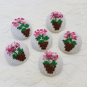 May include: Six handmade embroidered buttons featuring pink flowers in brown pots on a white background. The buttons are approximately 1 inch in diameter.