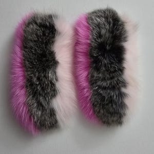 May include: Two fluffy fox fur pom poms with pink, gray, and white stripes. The pom poms are soft and fluffy and would be perfect for adding a touch of luxury to any project.