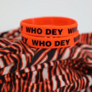 May include: Two orange silicone wristbands with the text "WHO DEY" in black lettering.