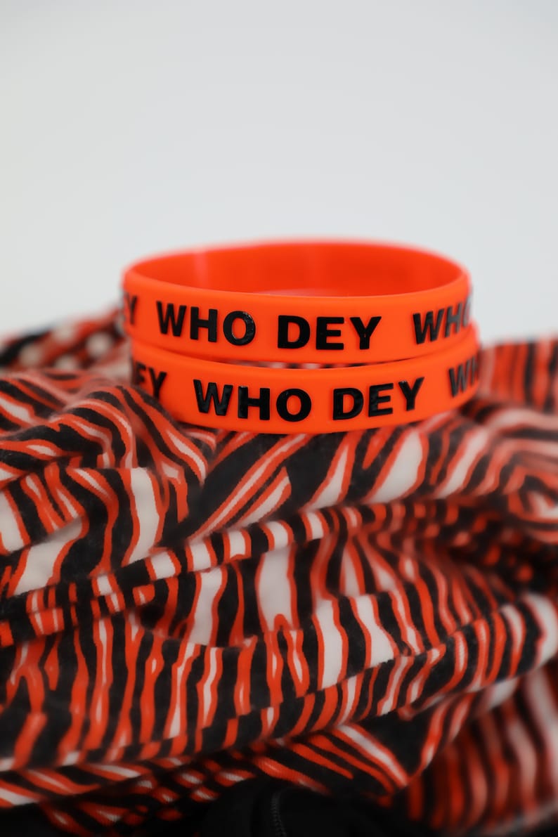 May include: Two orange silicone wristbands with the text "WHO DEY" in black lettering.