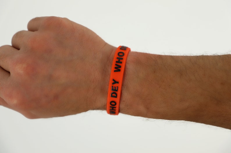 May include: Orange silicone wristband with the text "WHO DEY WHO" in black.