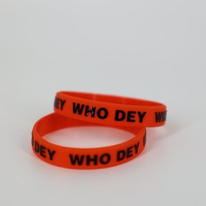 May include: Two orange silicone bracelets with the text "WHO DEY" printed in black.