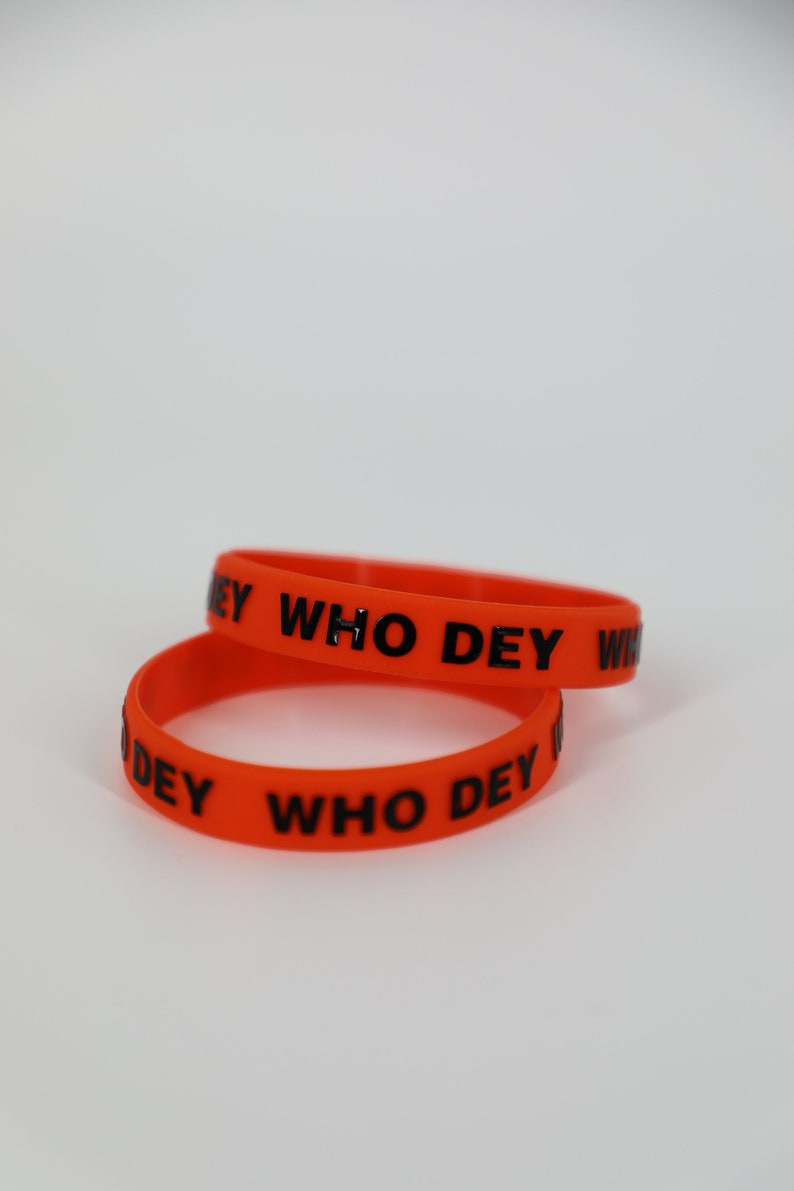 May include: Two orange silicone bracelets with the text "WHO DEY" printed in black.