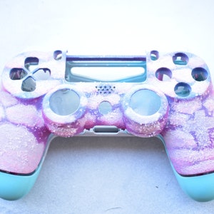 Może przedstawiać: Spersonalizowany kontroler do gier w pastelowej kolorystyce. Posiada marmurkowy wzór w odcieniach różu, fioletu i bieli, z błyszczącym wykończeniem. Dolne uchwyty są w kolorze jasnoniebieskim.