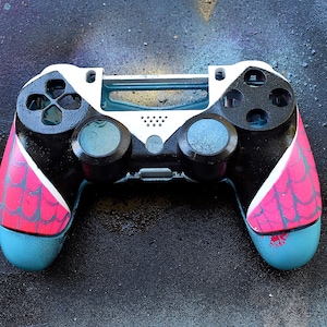 Könnte beinhalten: Ein schwarzer und weißer PlayStation 4-Controller mit rosa und blauen Akzenten. Der Controller hat ein strukturiertes Design an den Griffen.