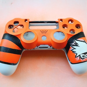 Könnte beinhalten: Ein individuell lackierter orangefarbener und schwarzer PlayStation 4-Controller mit einem weißen Design auf der rechten Seite. Der Controller hat ein Tigerstreifenmuster auf der linken Seite.