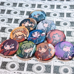 May include: A set of ten round pins featuring colorful illustrations of anime characters. The pins are arranged in a pyramid shape on a background of black and white camera illustrations.