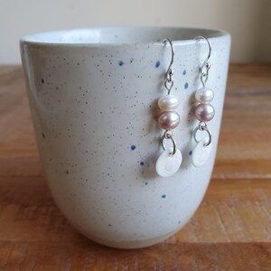 May include: A pair of silver dangle earrings with pink and white pearl beads and white ceramic charms.