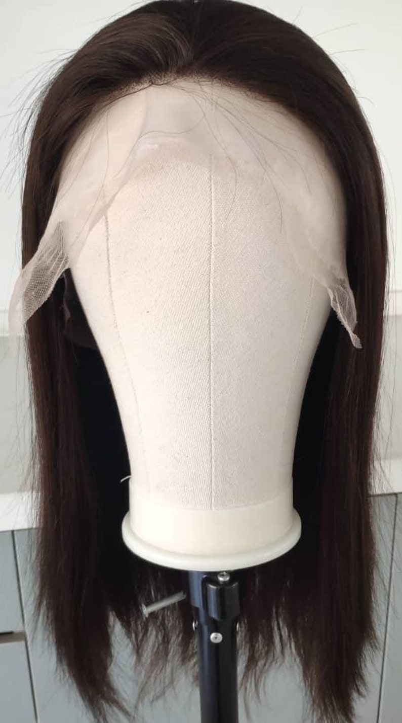 May include: A dark brown human hair wig on a mannequin head with a lace front. The wig is straight and has a blunt cut.