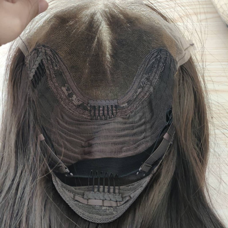May include: The back of a brown wig with a lace front and adjustable straps. The wig has a brown mesh cap with clips and an elastic band.