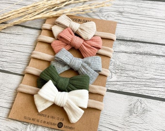 May include: Set of five nude, pink, gray, green, and white ribbed fabric headbands with matching bows. The headbands are displayed on a brown card with the text "BBIN BAY" and "HANDMADE IN CRAIG, CO, USA" and "FOLLOW AND TAG US ON INSTAGRAM BOBBINBAY".