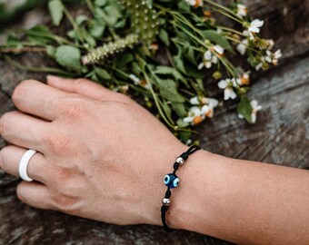 May include: A black string bracelet with a silver bead and a blue evil eye charm.