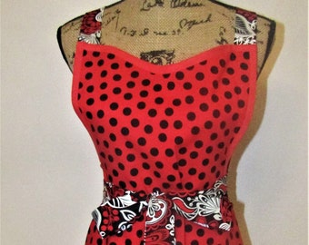 May include: Red and black polka dot apron with a floral print waistband and pockets. The apron has a sweetheart neckline and adjustable straps.
