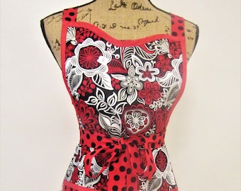May include: A red and black floral print apron with a red polka dot trim and matching tie. The apron has two large pockets on the front.
